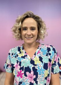 Smiling person in floral scrubs against a gradient background.