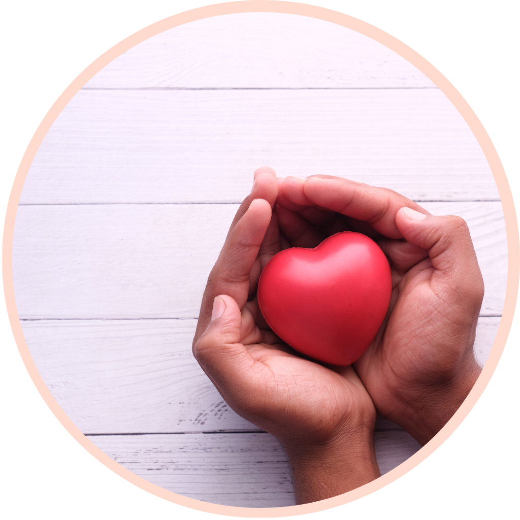 Hands holding a red heart on wood background.