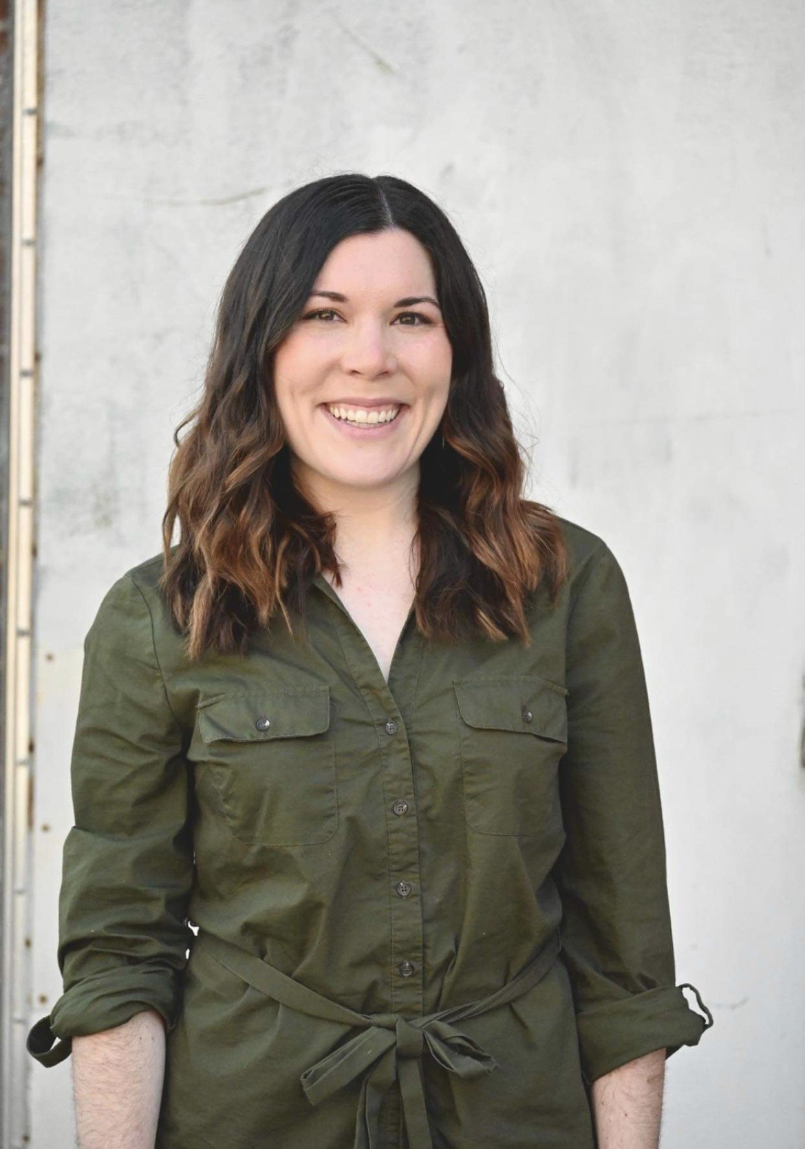 Smiling woman in green shirt against white wall.