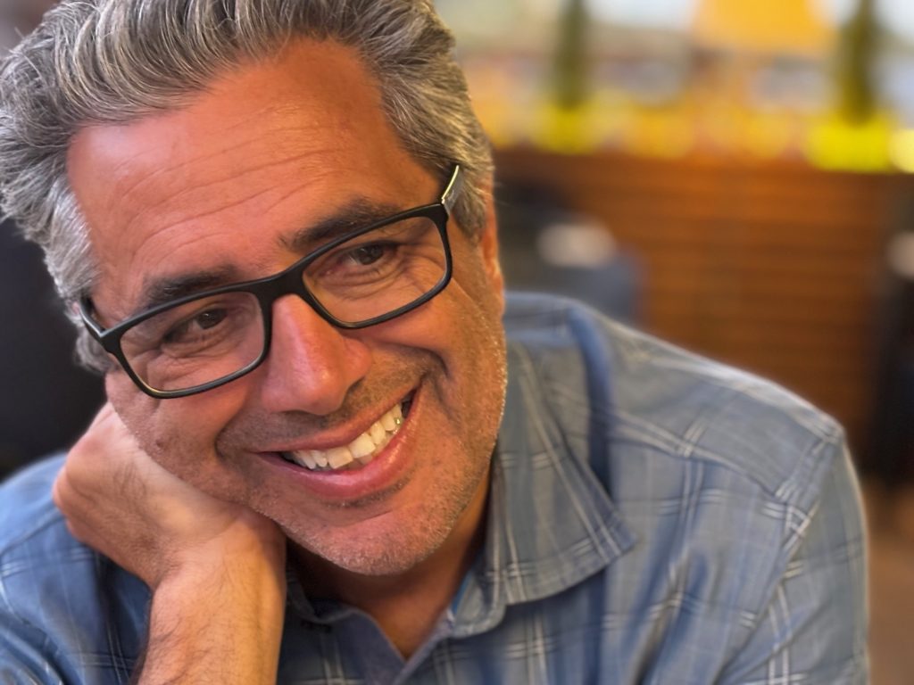 Man in glasses smiling, wearing blue shirt.